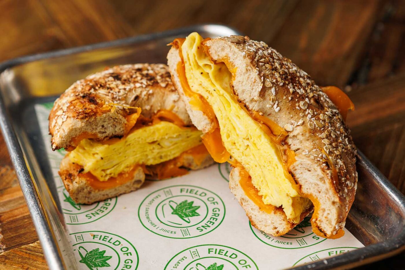 breakfast sandwich, cut in two and positioned on a tray with Field of Greens paper below it