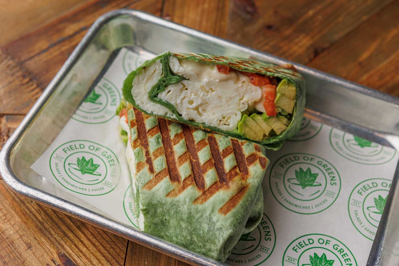 sandwich cut in two, atop a tray with Field of Greens-branded paper